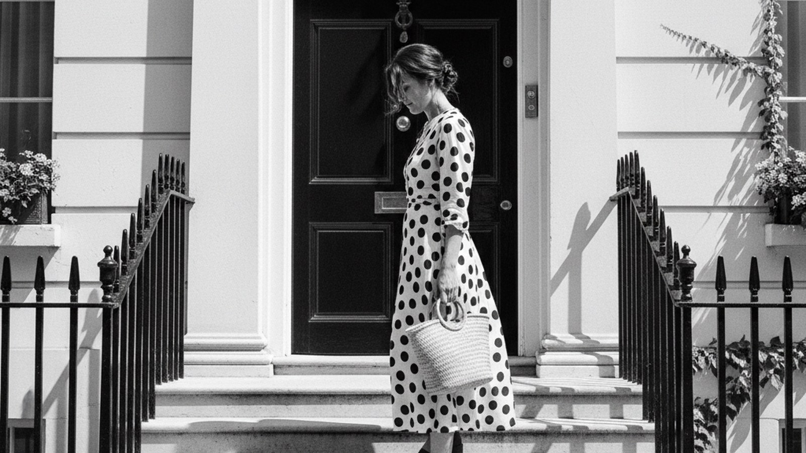 Woman in polka dot dress standing on Georgian stone steps, face in three-quarter profile, hair pinned up, black and white pho