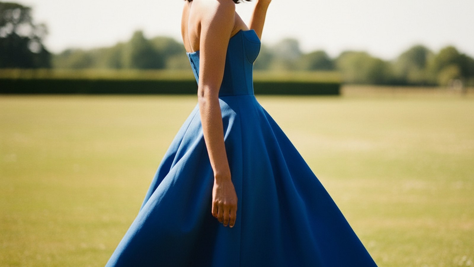 Woman in cobalt blue midi dress and cream straw hat, glancing over her shoulder in bright midday sunlight.