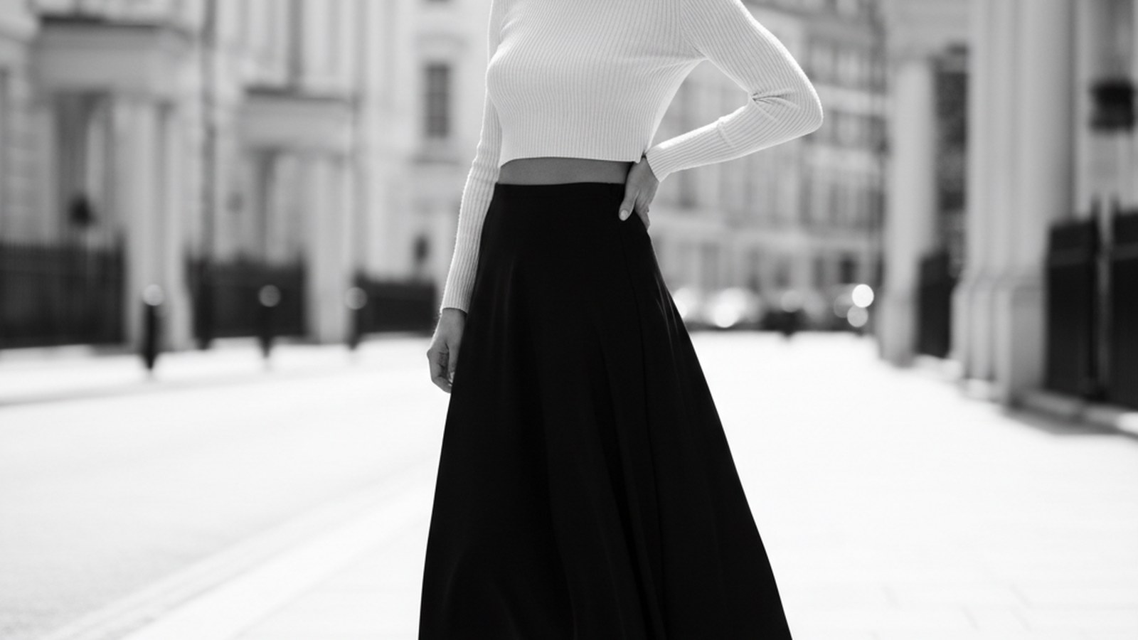 Woman in cream cropped ribbed knit and fluid black drop-waist midi skirt with white leather trainers, standing on a London st