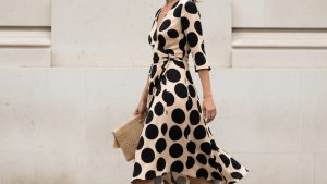 Woman walking along a London street in a cream bias-cut midi dress with large black polka dots, hem lifting in the breeze, ho