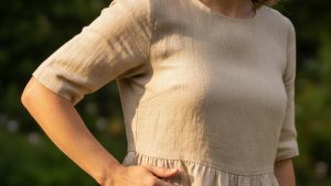 Woman smoothing a crease in an ecru linen dress with her right hand, shot from waist to shoulder in warm natural light.