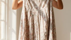 Woman holding up a crumpled, distorted floral viscose midi dress with an uneven, puckered hemline suggesting shrinkage.