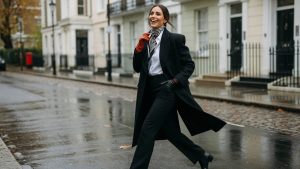 Neutral autumn wardrobe staples on a rail: wool coat, knitted jumper, tailored trousers and leather boots