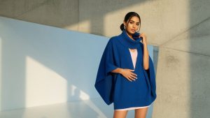 A cobalt blue knitted cape jumper styled with wide-leg tailored trousers and tan ankle boots
