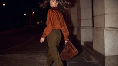 Woman walking through airport terminal in wide-leg trouser-jogger hybrid trousers with matching-tone loafers and structured tote
