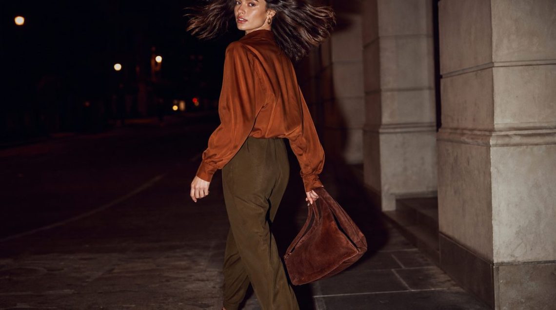 Woman walking through airport terminal in wide-leg trouser-jogger hybrid trousers with matching-tone loafers and structured tote