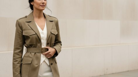 Utility Trend Summer 2026: The Pieces That Work in Britain Woman in sand-khaki belted utility jacket over white silk vest and ivory wide-leg trousers, standing on a London pavement.