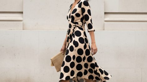 Woman walking along a London street in a cream bias-cut midi dress with large black polka dots, hem lifting in the breeze, ho