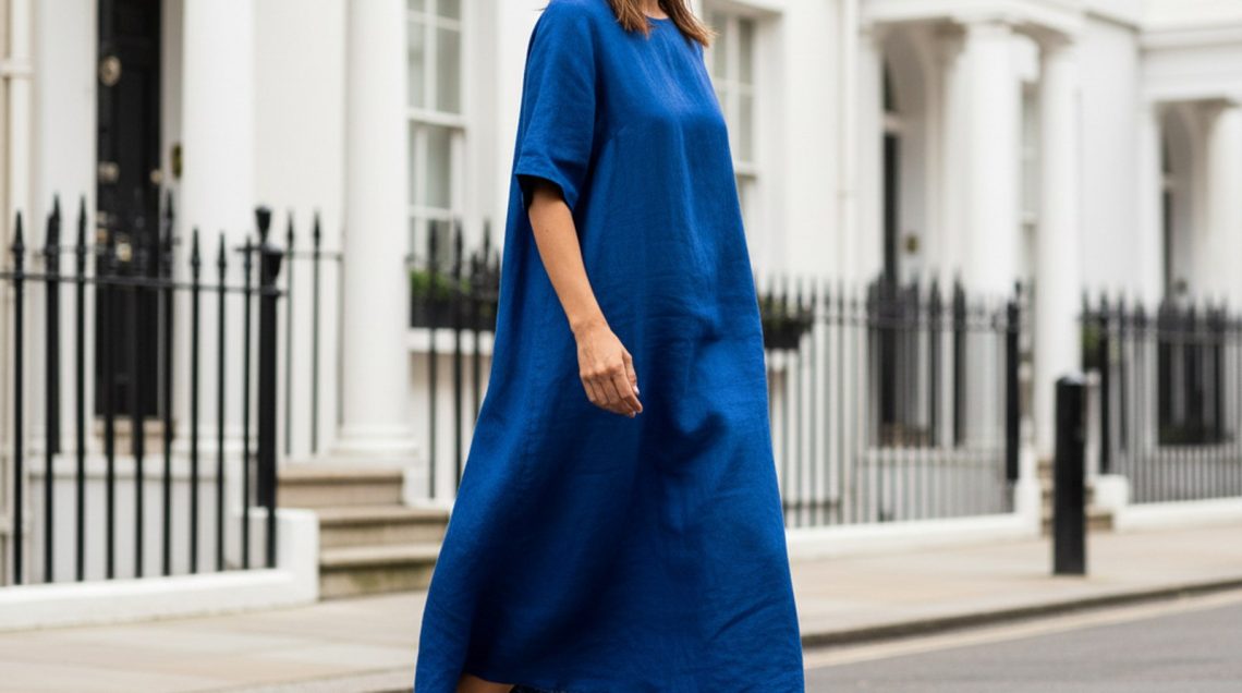 The Linen Trousers Outfit Formula That Solves British Summer Dressing Woman walking in garden wearing cream wide-leg linen trousers and ivory silk blouse, light brown hair falling across her face