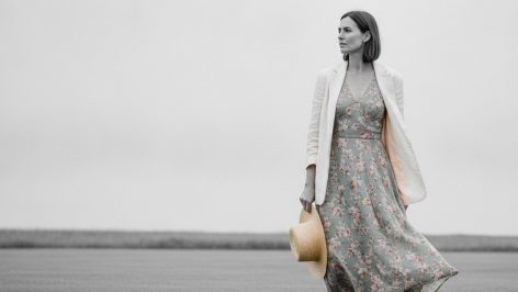 What to Wear Over a Summer Dress in the UK: The 3-Piece Capsule Woman in floral midi dress and open ivory linen blazer stands on a green country lawn, gazing off-camera.