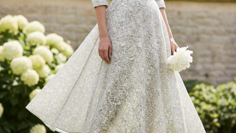 Cotton Lawn vs Voile: What Actually Happens in UK Summer Heat Woman in floral midi cotton lawn dress, pale ivory and grey print, fabric lifting lightly in breeze, sunlit walled garden.