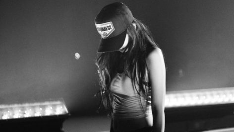 Jennie from Blackpink kneeling on stage in a black and white photo, wearing a Dsquared2 cap and a crop top during Gov Ball rehearsals.