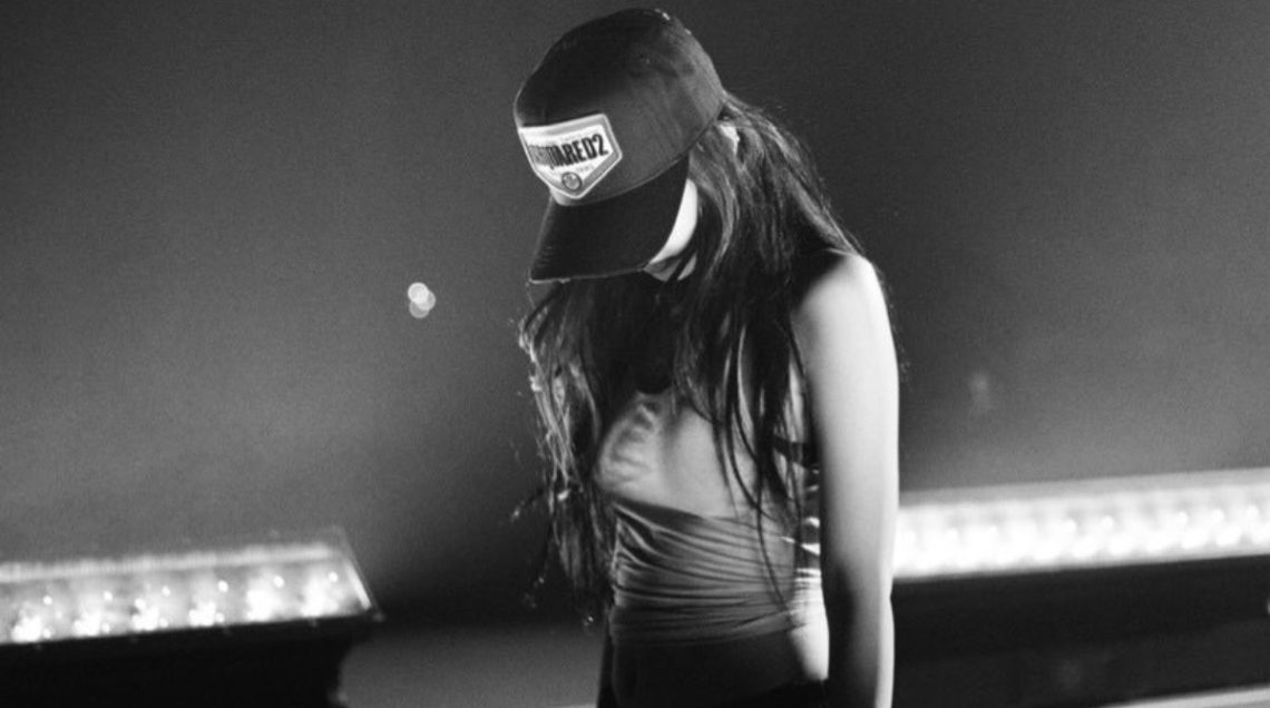 Jennie from Blackpink kneeling on stage in a black and white photo, wearing a Dsquared2 cap and a crop top during Gov Ball rehearsals.